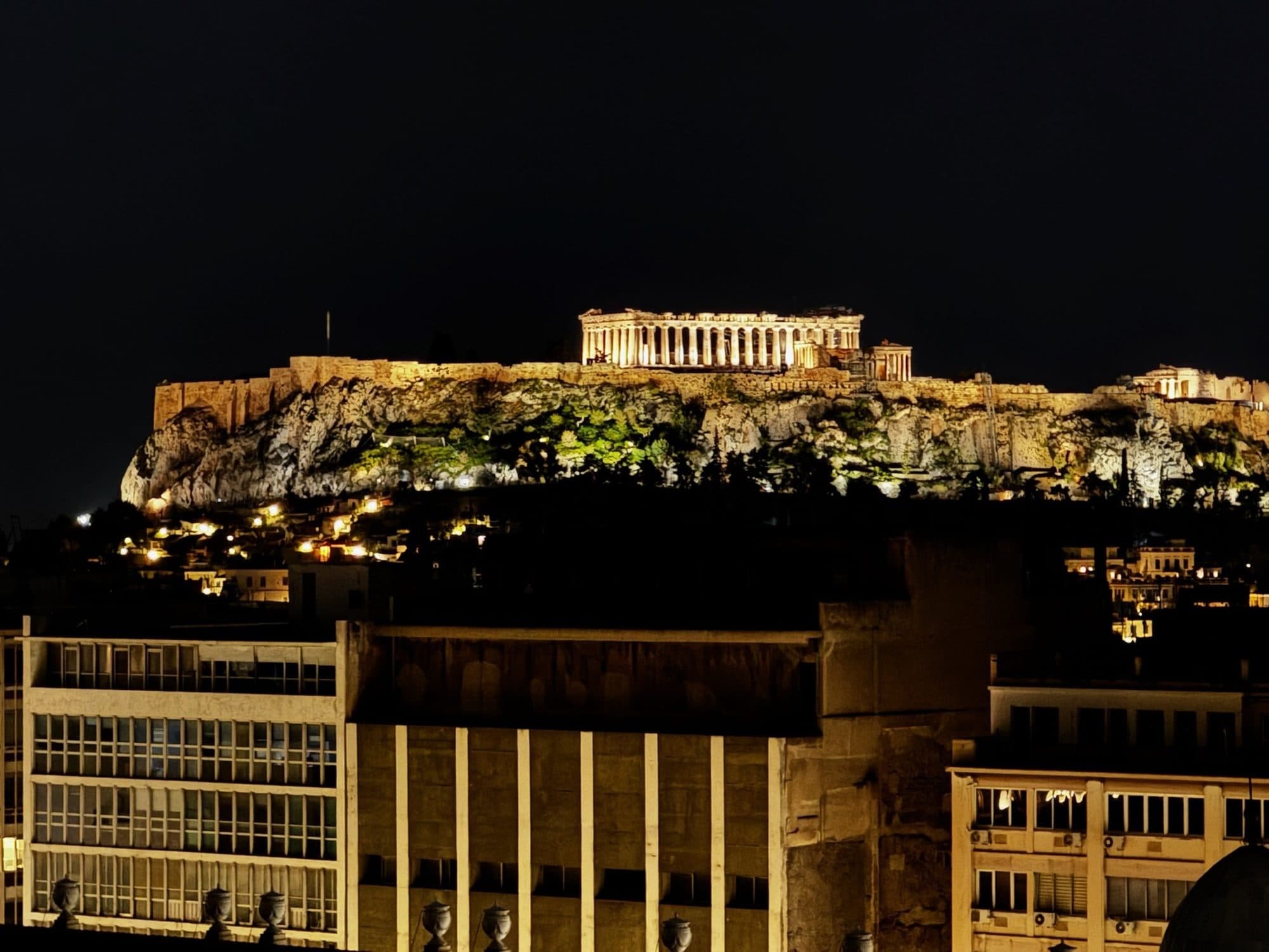 Ancient ruins lit at night beneath a hillside city